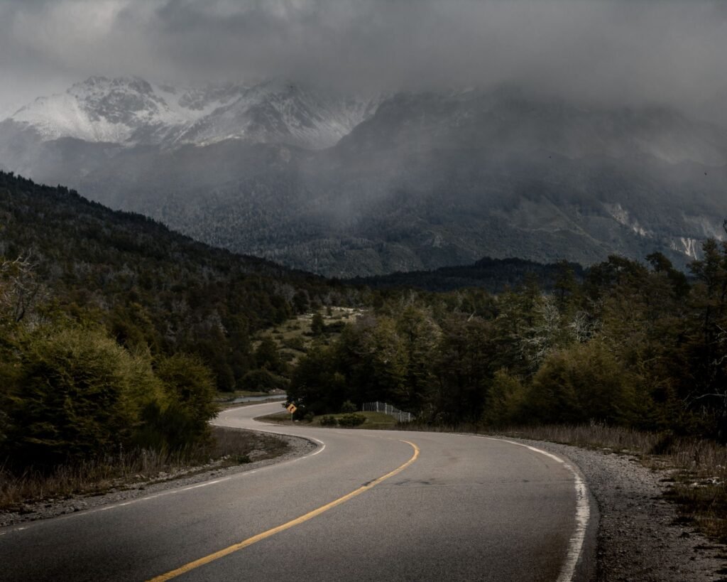 Camino curvo entre bosque verde y montañas nevadas envueltas en niebla